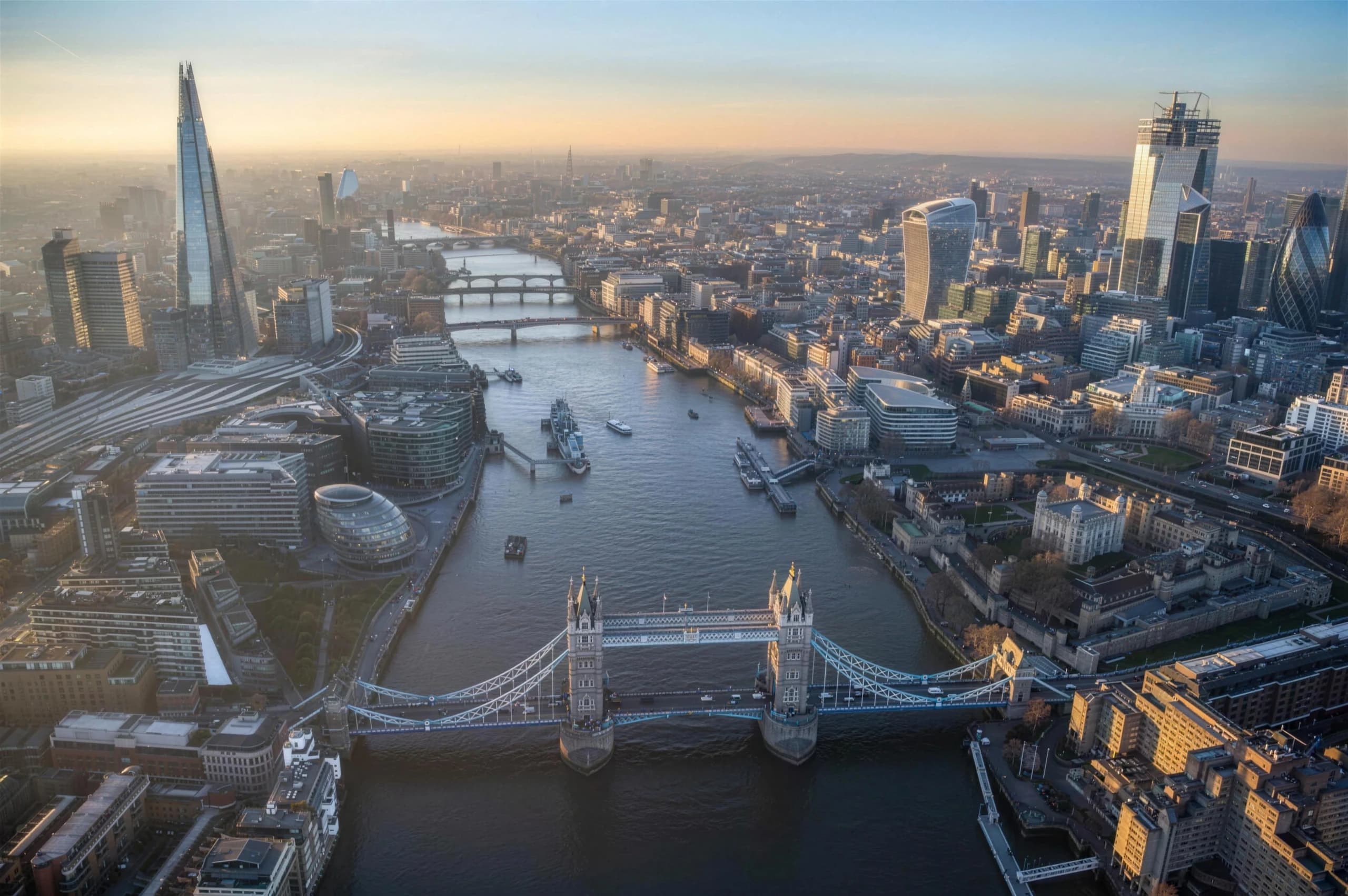 Aerial view of London, with Tower Bridge over the Thames, the Shard and the City skyline in golden light.
